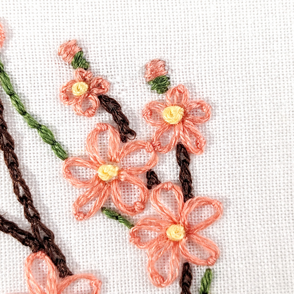 Close-up view of peach blossom flowers stitched in white fabric.
