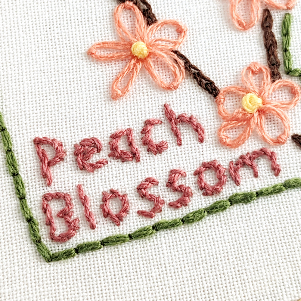 The words Peach Blossom stitched on white fabric.