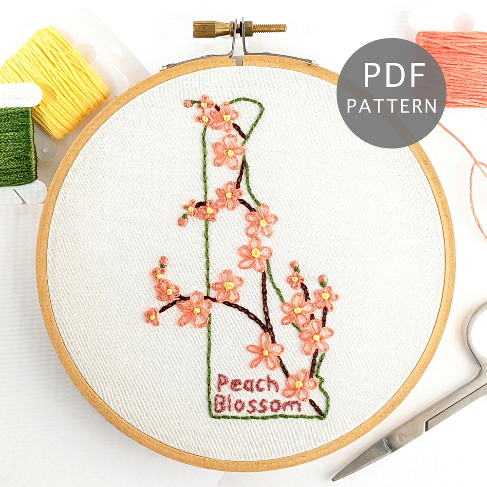 Branch filled with peach blossom flowers stitched on white fabric inside the Delaware state outline.