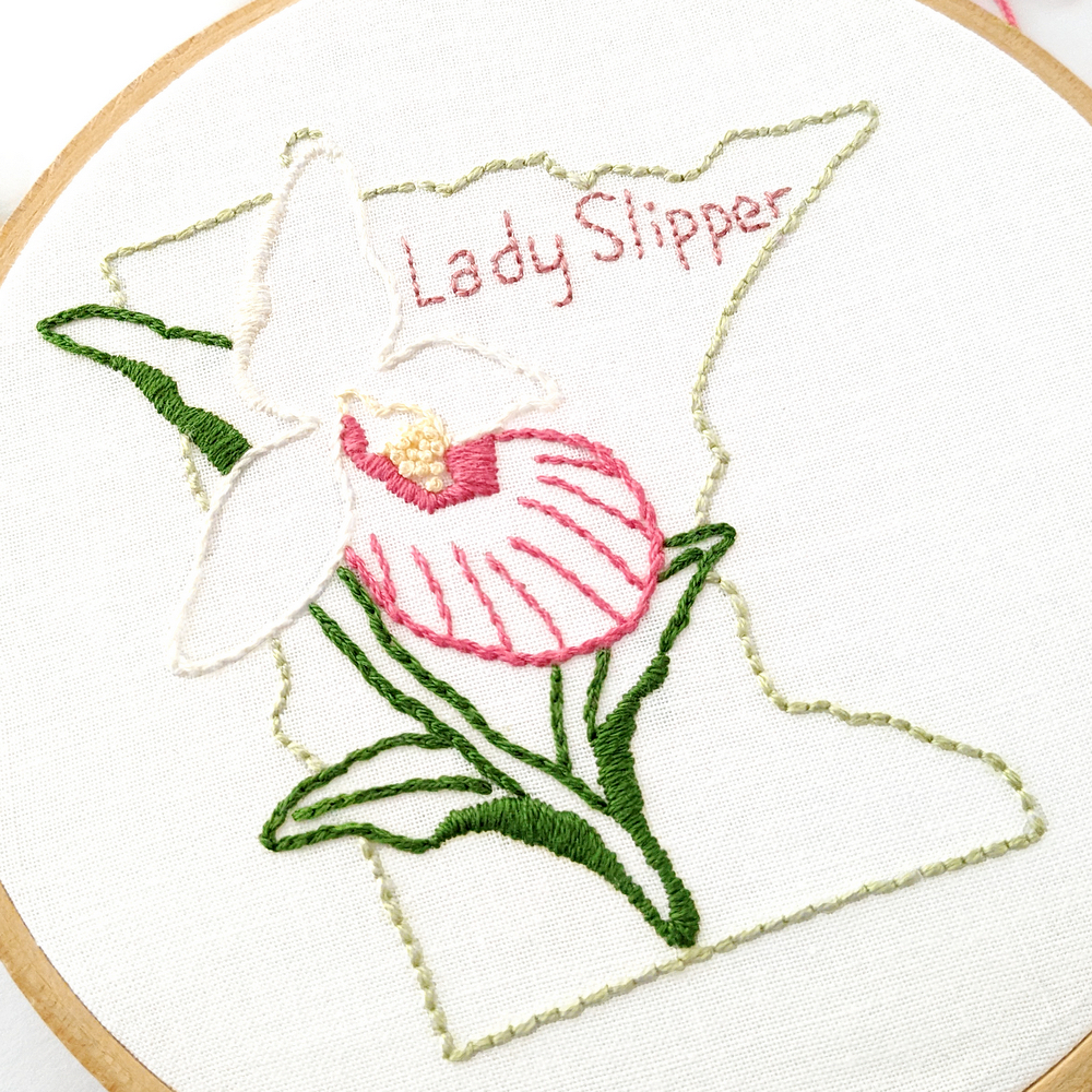 Lady Slipper flower stitched on white fabric inside the Minnesota state outline.