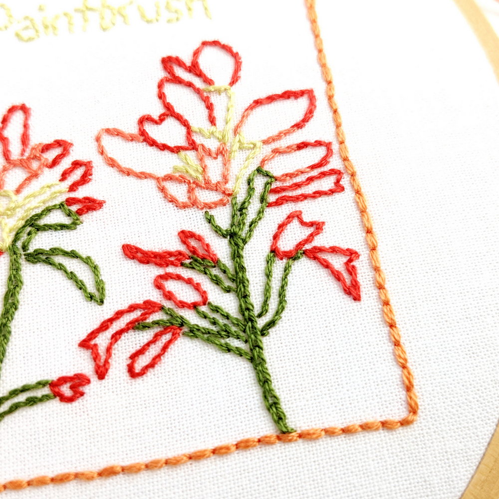 Close-up of Indian Paintbrush flowers stitched on white fabric inside the Wyoming state outline