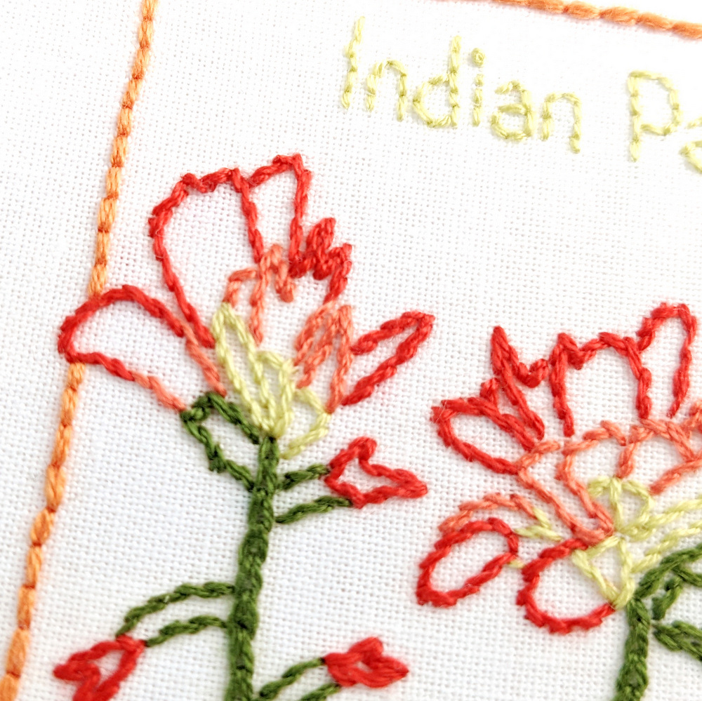 Close-up of Indian Paintbrush flowers stitched on white fabric inside the Wyoming state outline