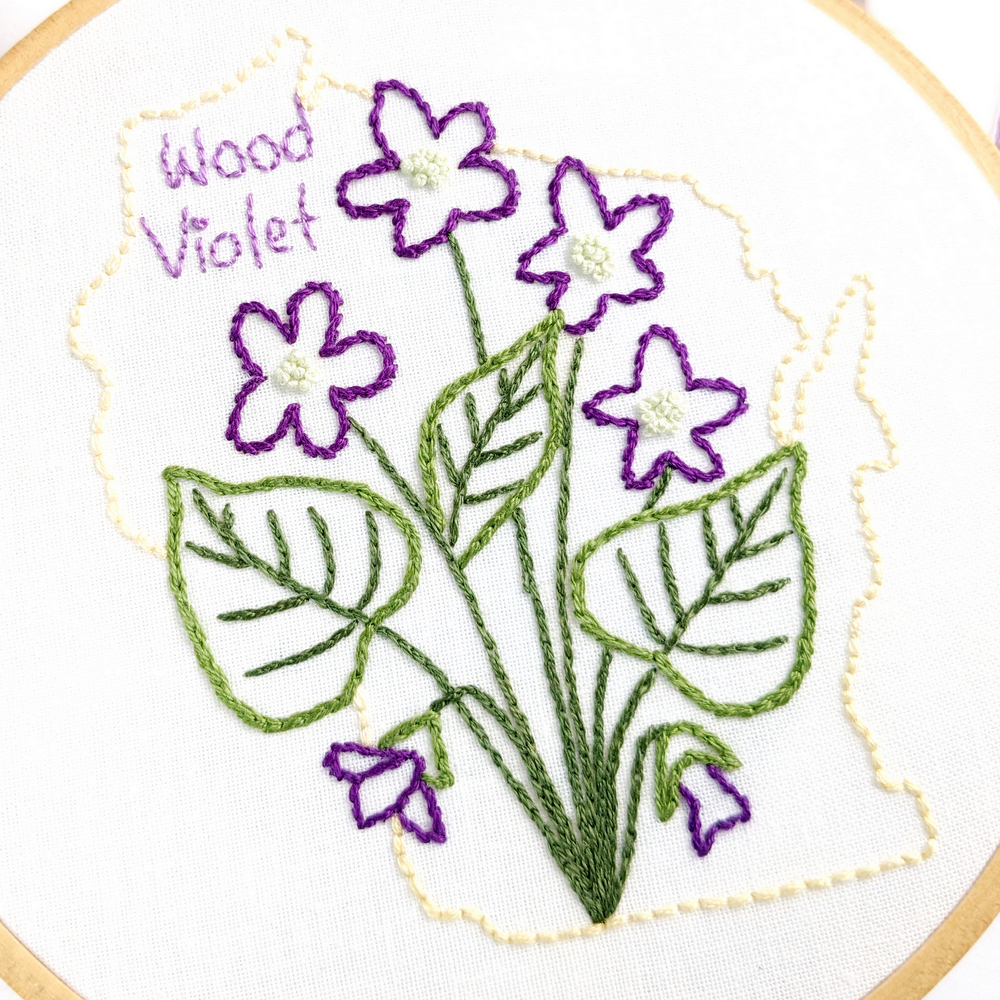 Wood Violet flower stitched on white fabric inside the Wisconsin state outline.
