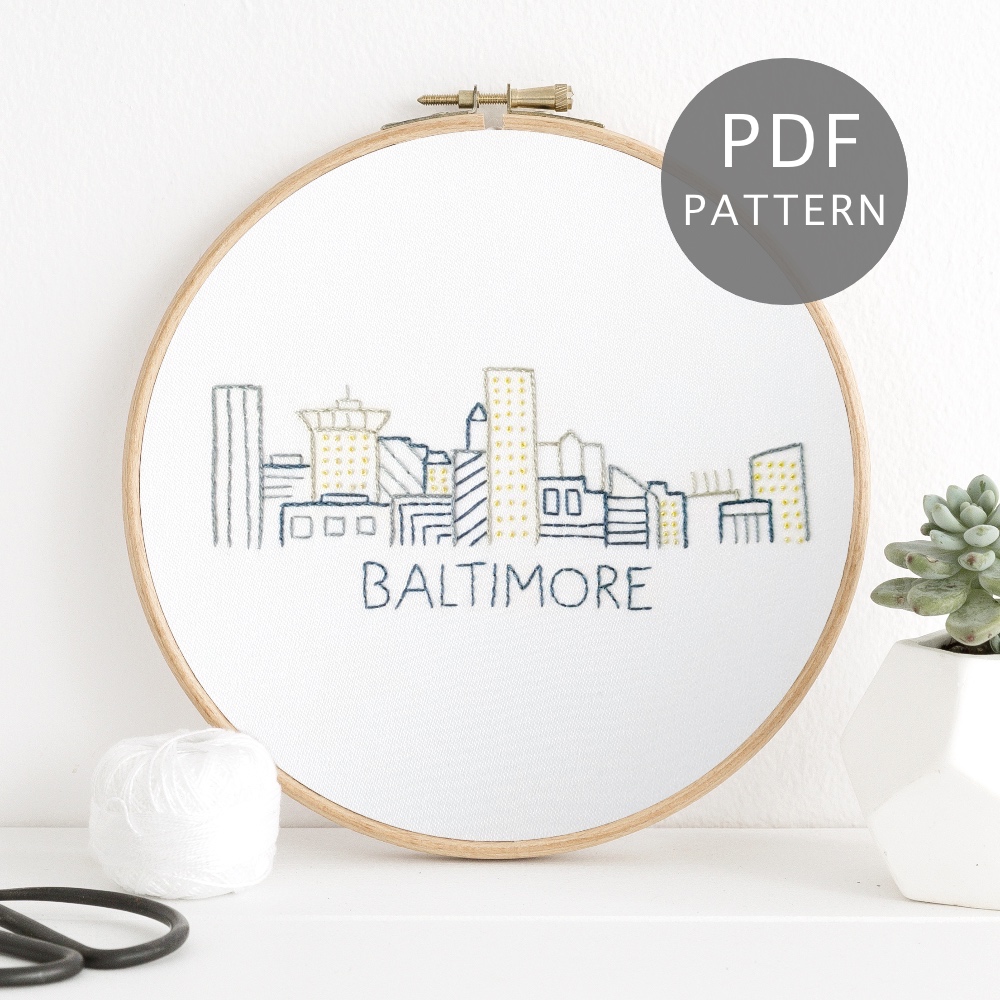 Baltimore city skyline stitched on white fabric inside a wooden frame.