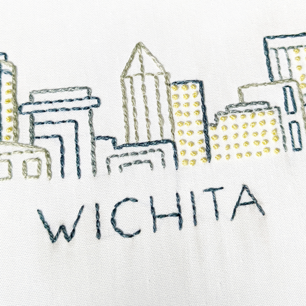 Close-up view of the Wichita skyline hand stitched on white fabric.