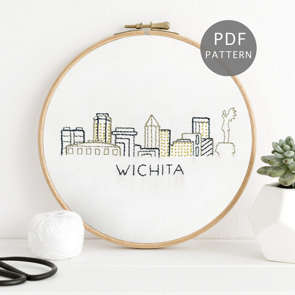 Wichita skyline hand stitched on white fabric inside a wooden hoop.