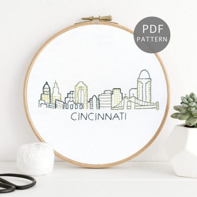 Cincinnati skyline hand stitched on white fabric inside a wooden hoop.