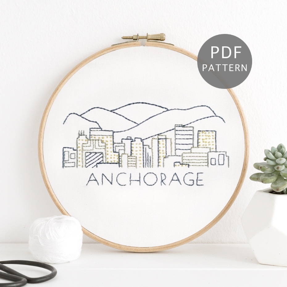Anchorage city skyline stitched on white fabric inside a wooden frame.