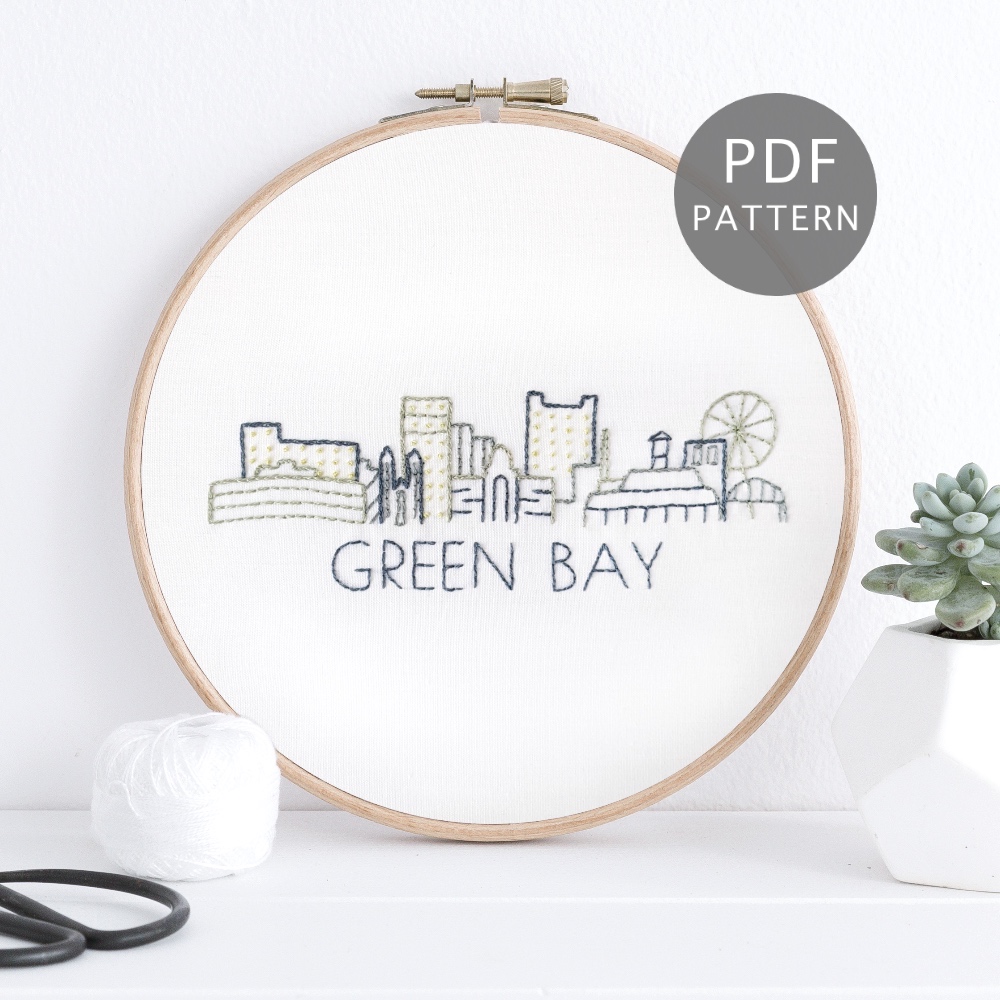 Green Bay city skyline stitched on white fabric inside a wooden frame.