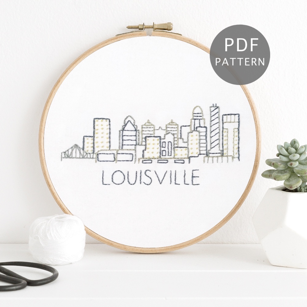 Louisville city skyline stitched on white fabric inside a wooden hoop.