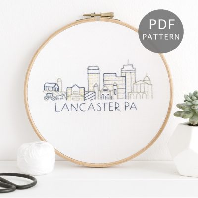 Lancaster, PA city skyline stitched on white fabric inside a wooden hoop.
