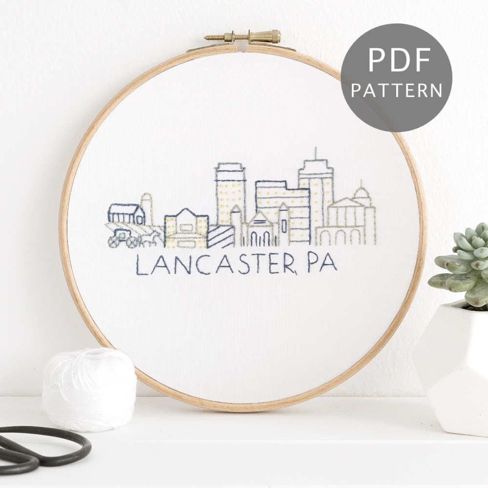 Lancaster, PA city skyline stitched on white fabric inside a wooden hoop.